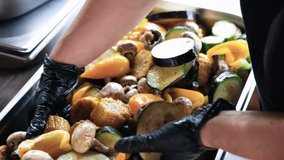 A cook in black gloves stirs grilled vegetables to evenly distribute oil, spices and marinade. Slow motion horizontal video