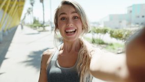 Young blonde woman wearing sportswear having video call at street