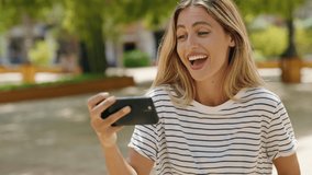Young blonde woman smiling confident watching video on smartphone at park