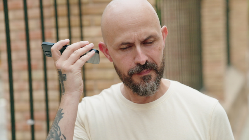 Young bald man smiling confident listening audio message by the smartphone at street