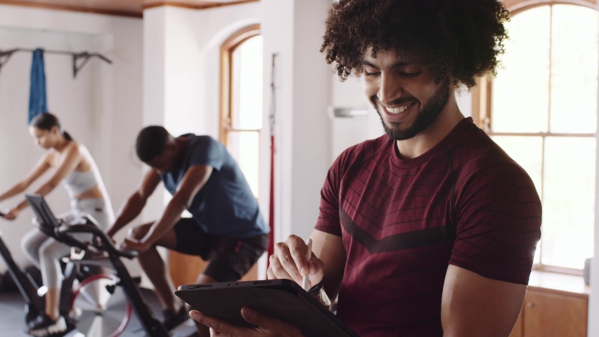 Cheerful Middle eastern young adult male, fitness professional using tablet and pen while at an indoor fitness gym