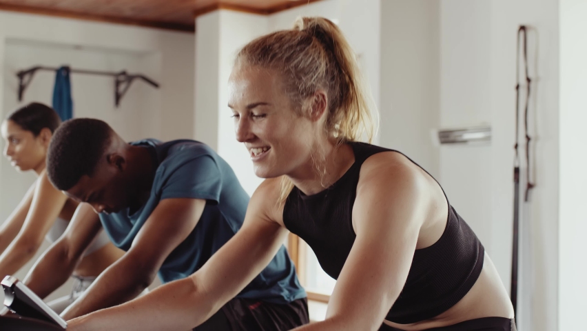 Caucasian female cycling on stationary bike in a group fitness class at an indoor fitness gym. Having a good time and determined. Royalty-Free Stock Footage #1095097679