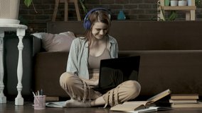 Girl is doing homework in living room with laptop on floor next to books and textbooks. student with headphones is studying online at home. school girl is typing on laptop preparing for college exams