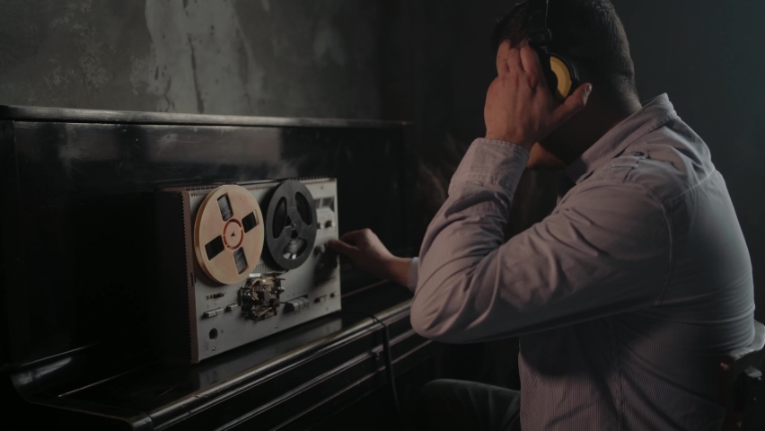 Secret agent listens on the reel tape recorder. Officer wiretapping in headphones. Spying of conversations. Intelligence gathering. Espionage concept. Report information to superiors. Royalty-Free Stock Footage #1095100283