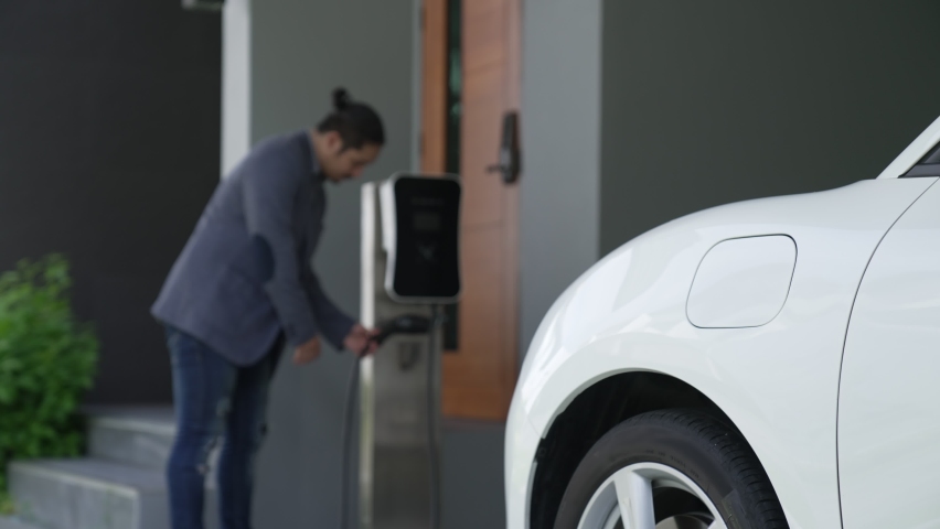 Progressive man attaches an emission-free power connector to the battery of electric vehicle at his home. Electric vehicle charging via cable from charging station to EV car battery Royalty-Free Stock Footage #1095105135