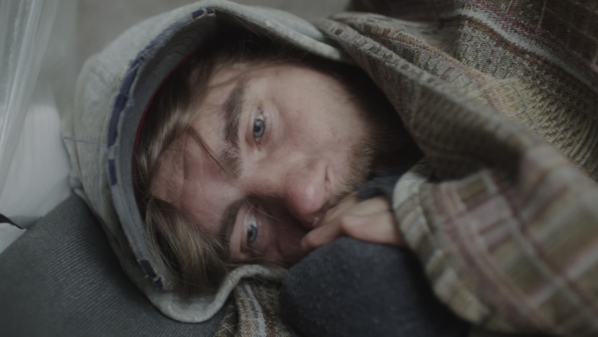 Close up shot of homeless man pulling blanket over face and sleeping on ground on cold day | Shutterstock HD Video #1095108385