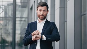 Professional confident businessman standing outdoors waiting for meeting looks at wristwatch checking time displeased caucasian man pointing on watch looking at camera dissatisfied with being late - Powered by Shutterstock - Get 15% off with code: PIKWIZARD15