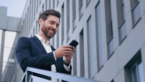 Stylish handsome businessman holding phone reading email stands on street smiling writes message communicates in social network pensive man browses goods in online store using mobile app on smartphone - Powered by Shutterstock - Get 15% off with code: PIKWIZARD15