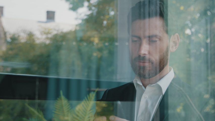 Close up reflection in glassy window blue glass Caucasian bearded 40s middle-aged man adult businessman walking indoor in office company browsing scrolling phone mobile app looking outside pensive Royalty-Free Stock Footage #1095108481