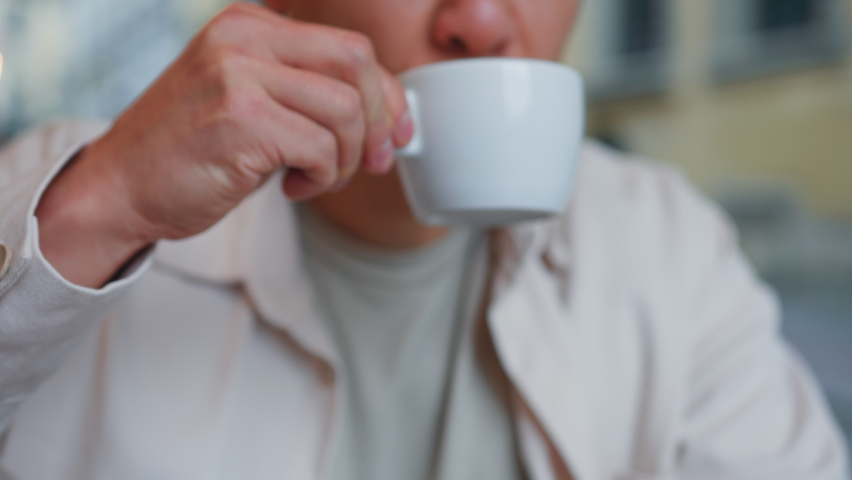 Close-up focus on cup relaxed man sits in cafe drinks coffee enjoys fragrant drink asian businessman resting in cafeteria weekend sitting at table drinking hot tea enjoying morning espresso relaxing | Shutterstock HD Video #1095108489