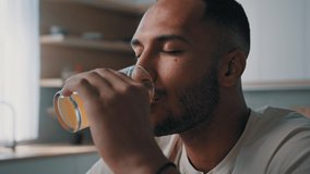 30s sportsman male African guy man athlete in white T-shirt sits at home in kitchen breakfast drinks orange juice vitamins food supplements calcium glass of drink fresh healthy nutrition refreshment - Powered by Shutterstock - Get 15% off with code: PIKWIZARD15