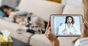 Close up of Caucasian woman videochatting with female physician while sitting at home. Mother having online video call with doctor who shows medicines. Sick small girl laying on sofa Treatment concept