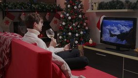 A guy with glasses on a video call with girlfriend and drinking some sparkling wine. A man drinking champagne with a fireplace on the background on Christmas.