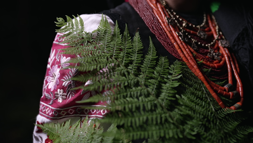 Authentic woman in traditional ukrainian necklace, costume with fern in forest at night. Lady in national dress - vyshyvanka, ancient coral beads. Concept of witch.