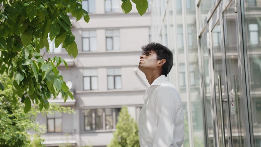 Medium closeup of successful businessman observing tree outside building