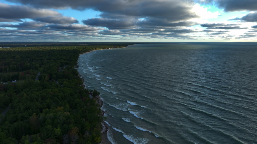 Aerial Drone Footage of the shore of Lake Huron in East Tawas, Michigan. Taken during sunrise in early Fall, some leaves are changing colors. Windy day with waves crashing upon the sandy shore.