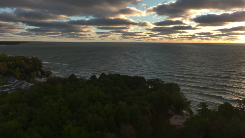 Aerial Drone Footage of the shore of Lake Huron in East Tawas, Michigan. Taken during sunrise in early Fall, some leaves are changing colors. Windy day with waves crashing upon the sandy shore.