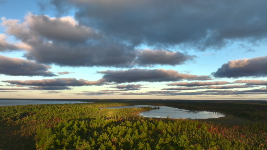 Aerial Drone Footage of the shore of Lake Huron in East Tawas, Michigan. Taken during sunrise in early Fall, some leaves are changing colors. Windy day with waves crashing upon the sandy shore.