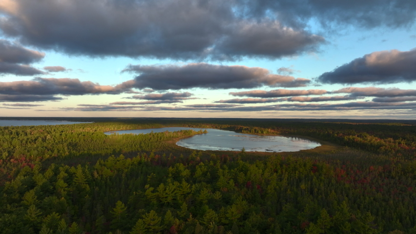 Aerial Drone Footage of the shore of Lake Huron in East Tawas, Michigan. Taken during sunrise in early Fall, some leaves are changing colors. Windy day with waves crashing upon the sandy shore.