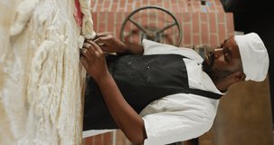 Vertical video of african american male baker preparing dough in bakery. global business and bakery.