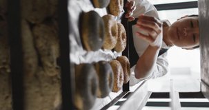 Vertical video of happy asian female baker preparing donuts in bakery. global business and bakery.