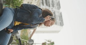 Vertical video of happy african american woman wearing headphones in city. digital nomad on the go.