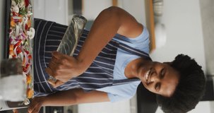 Vertical video of happy african american woman cooking at home. spending time alone at home.