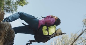 Vertical video of happy african american woman with backpack hiking in countryside, enjoying view. healthy, active outdoor lifestyle and leisure time.