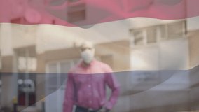 Animation of flag of netherlands waving over african american man wearing face mask in city street. global health precautions during covid 19 pandemic concept digitally generated video.