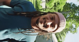 Vertical video of smiling biracial man with dreadlocks and hat smiling to camera. body inclusivity, positivity and healthy lifestyle.