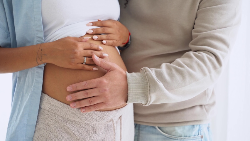 Closeup couple expecting a baby while husband caresses the belly of his pregnant multiethnic woman. Lovely white man touching belly of his girlfriend and feeling baby movement. | Shutterstock HD Video #1095125571
