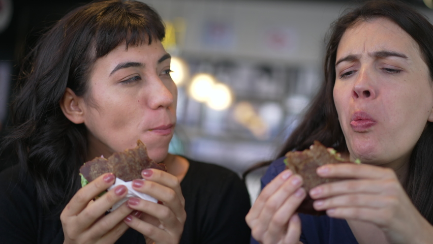 People eating fast food for lunch at restaurant. Two women holding hamburgers