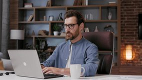 Handsome male businessman manager working tiredly behind a laptop in a stylish home office. Loss of vision from the screen. Fatigue and burnout from work. Overwork and stress.