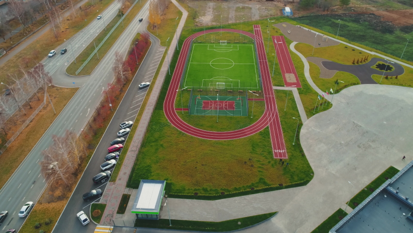 Large sports ground with courts for ball games and jogging track in autumn city aerial view. Place for training and recreation