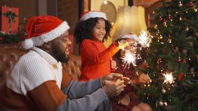 An African American black family, woman, father, mother and kid girl with spark sticks or cold fire, present gift in party on Merry Christmas Eve Xmas on holiday. Celebration at home. People lifestyle - Powered by Shutterstock - Get 15% off with code: PIKWIZARD15