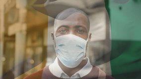 Animation of flag of ivory coast waving over latin man wearing face mask in city street. global health precautions during covid 19 pandemic concept digitally generated video.