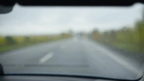 View from the interior of the car on 
windshield in rainy autumn weather.Wipers wash away raindrops and long road on background horizontal video. Travelling by car