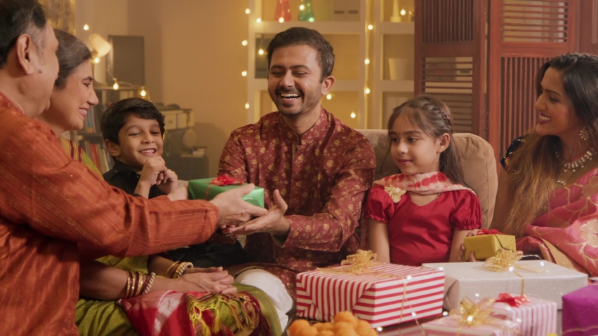 Ethnic Hindu Indian happy smiling family members sitting together and exchanging or giving gifts Boxes to each other on the occasion of Diwali festival or celebration in a well lit and decorated House Royalty-Free Stock Footage #1095145997
