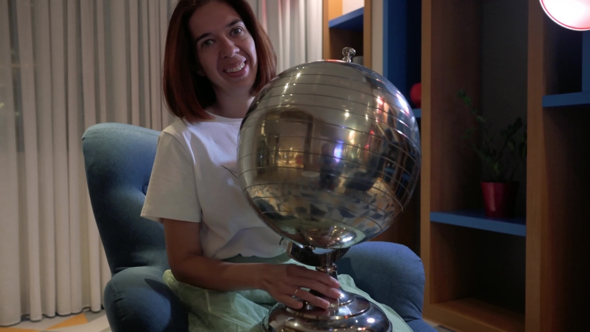 Woman sitting on a chair and rotating metal Earth globe. 4k footage UHD 3840x2160 