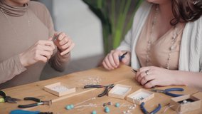 Two jewelry designers working in studio with tools and different gemstones making necklaces, bracelets and earrings. Female friends crafting jewellery together