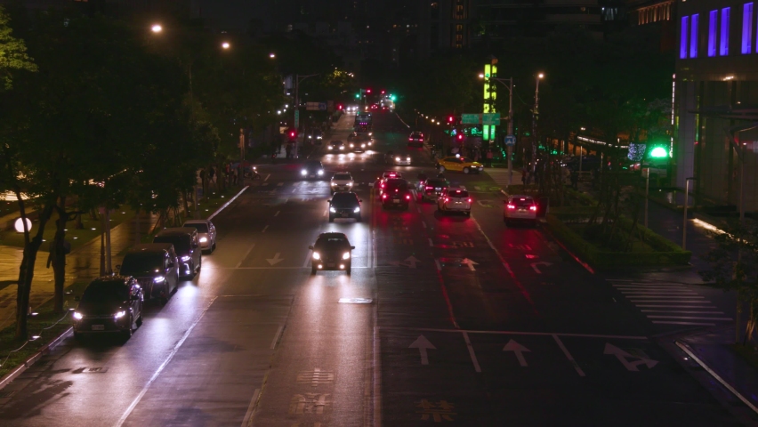 Street traffic at night in Taipei with cars and scooters with their headlights on – wide shot.