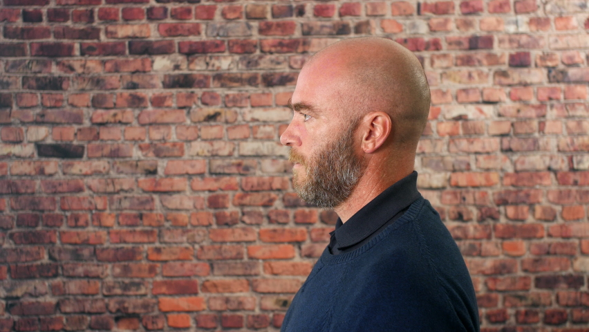 Side portrait of a man vaping indoors in front of a brick wall with cloud of smoke