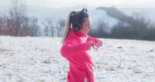 Run Woman, headphone girl runner on the snow in winter sunny day. Female in pink sportswear jacket fitness training outdoors, healthy lifestyle and vitamins, 4K slow motion video