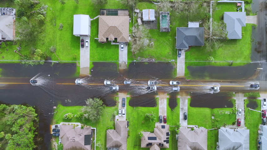 Hurricane Ian flooded street with moving cars and houses in Florida residential area. Natural disaster and its consequences