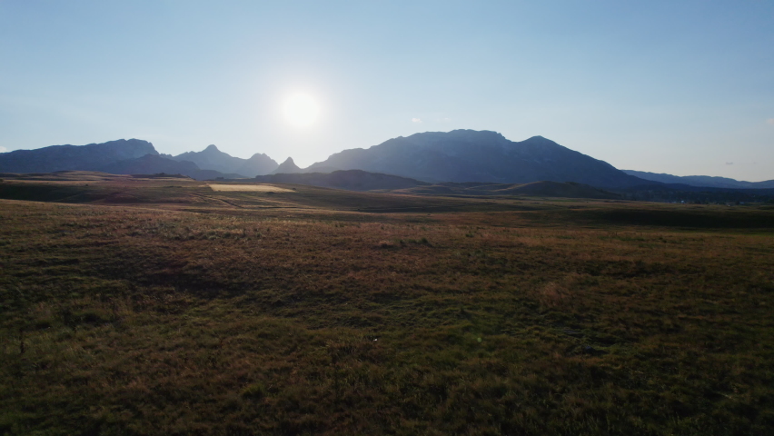 In flight over undulating meadows towards the Durmitor mountain range from a height towards sunset, edited with only minimal color correction