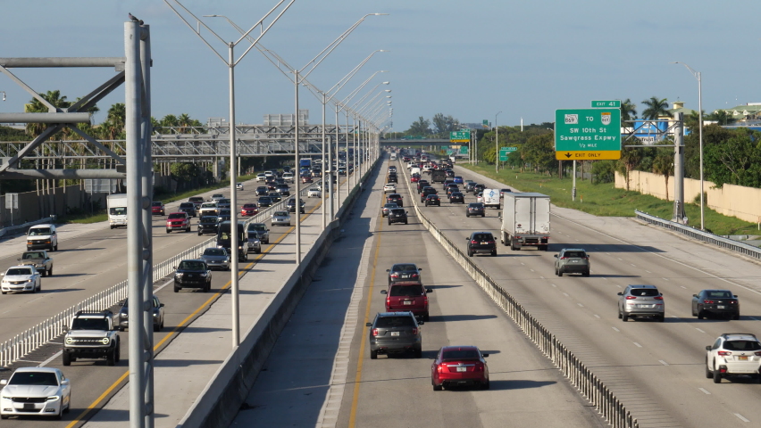 Traffic moves northbound and southbound along I-95 at 48th Street overpass near SW 10th Street in Deerfield Beach, Florida in late afternoon sun under clear blue sky.