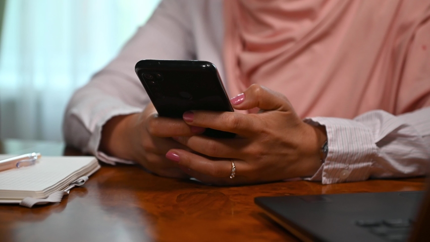 Cropped view. Selective focus on the hands of an unrecognizable Muslim woman, wearing a pink hijab, using smartphone, scrolling news feed, swiping, checking content in social media, networking | Shutterstock HD Video #1095180795
