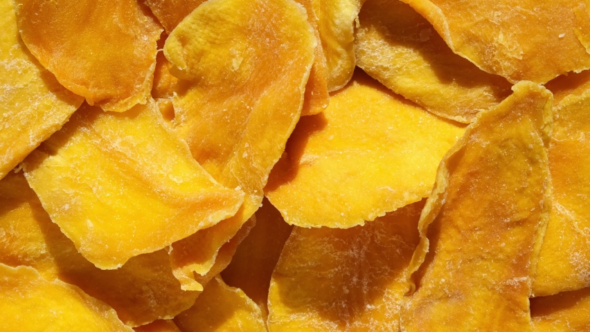 Dried mango slices close-up on a white. Top view. Closeup. Mango chips background. Dehydrated crispy fruit slices, pieces. Heap of sun-dried yellow fruit. Healthy meal. Top view, flat lay. 4K Footage.