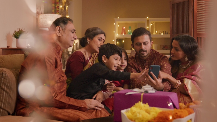 Happy smiling Hindu ethnic Indian family members in traditional clothes sitting together discussing or talking while online shopping using a mobile phone or smartphone during Diwali festival season. Royalty-Free Stock Footage #1095189719