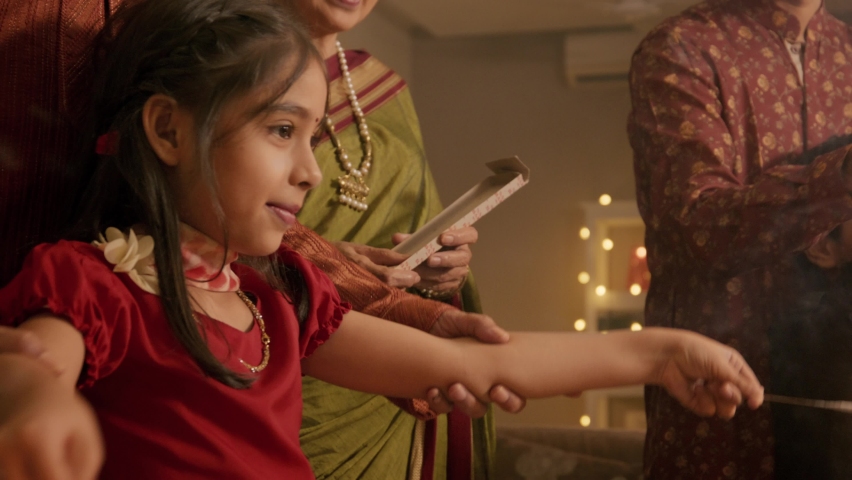Ethnic Indian Hindu happy smiling cute young girl or female kid in traditional clothes or attire playing with firecrackers or sparklers with the help of family elders or parents during Diwali festival Royalty-Free Stock Footage #1095190859